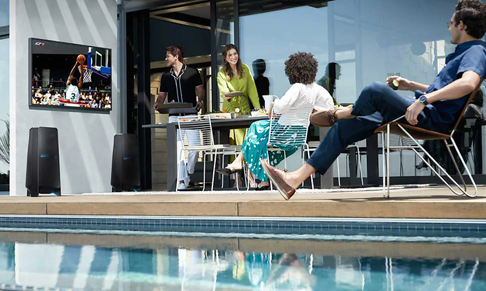 En person med några andra i bakgrunden tittar på The Terrace TV vid en pool medan mat serveras på bordet