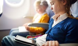 A young girl is sitting on an aeroplane reading an e-book next to a little girl