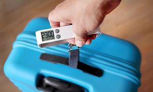 A hand is weighing a blue suitcase with a luggage weight