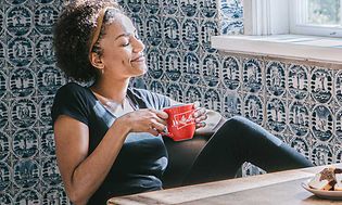 Kvinna som dricker från en kaffekopp och en kaffemaskin står på ett bord.