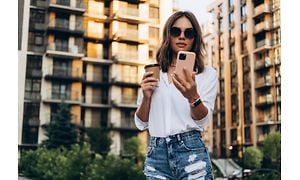 Kvinna med solglasögon som håller en kaffekopp och använder en smartphone