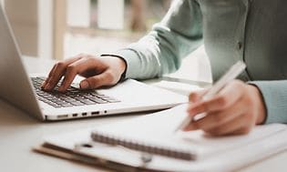 Kvinna som arbetar på en bärbar dator och skriver anteckningar
