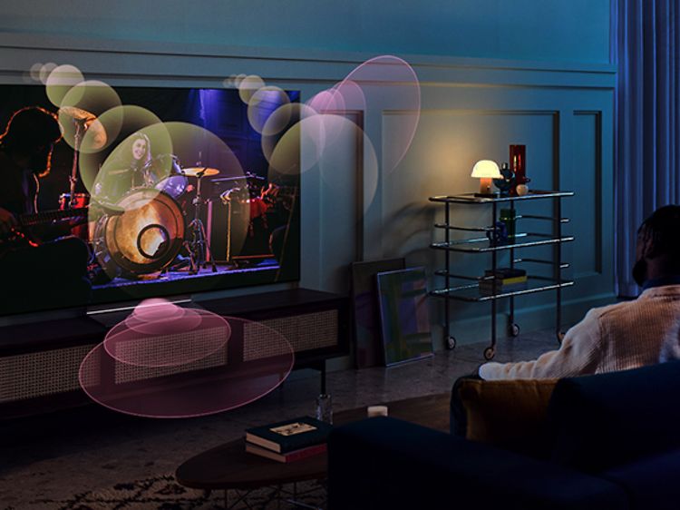 Ett par sitter i en soffa med en TV-skärm framför sig och illustrerade ljudvågor som kommer ur den från olika håll