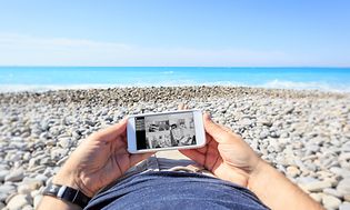 En man som ligger på stranden och tittar på sina övervakningskameror hemma