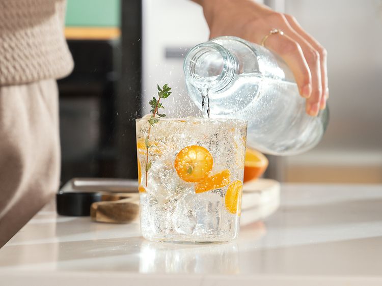 Person som häller kolsyrat vatten i ett glas