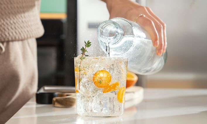 Person som häller kolsyrat vatten i ett glas