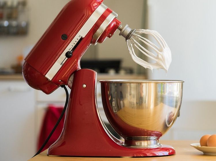 KitchenAid köksmaskin på ett bord, intill ägg och en plastbehållare med socker