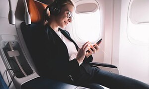 Kvinna kopplar av på ett flygplan med sin mobiltelefon och brusreducerande hörlurar 