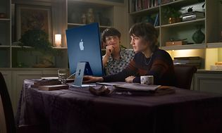 Två tonåringar i ett nedsläckt vardagsrum jobbar vid en iMac med M1-chip