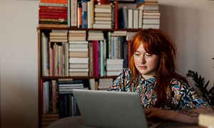 Kvinna som sitter med en macbook framför en bokhylla