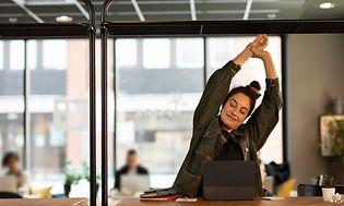 Kvinna som sitter i ett kontor och stretchar och ler