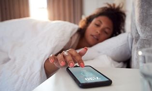 SDA-Alarm clocks- Woman in bed reaches Out To Turn Off Alarm On Mobile Phone