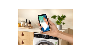 Hand holding a smartphone in front of a Electrolux washing machine