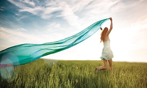 En kvinna springer i gräset och håller en lång turkos scarf som flyger i vinden