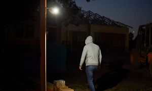 En Arlo Go V2 som lyser upp en garageuppfart på kvällstid och en man med luvtröja syns bakifrån