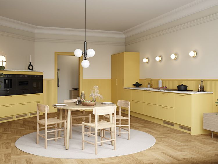 Öppet gult Epoq-kök med väggpanel, integrerad ugn och kaffemaskin och ett runt matbord av trä i mitten