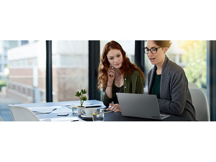 Två kvinnor sitter vid ett skrivbord och arbetar med en Lenovo ThinkBook-laptop
