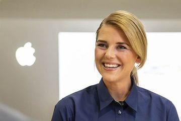 Leende kvinnlig Elgiganten-anställd bredvid en Apple-logotyp