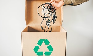 En hand som håller sladdar över en låda med grön återvinningssymbol
