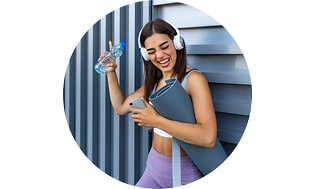 Glad kvinna med yogautrustning, vattenflaska och hörlurar håller smartphone och verkar lyssna på en bra låt