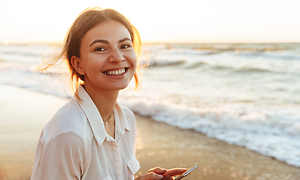 Elgiganten Services - Trade-in: Glad ung kvinna på en strand håller en smartphone