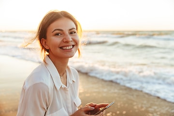 Elgiganten Services - Trade-in: Glad ung kvinna på en strand håller en smartphone