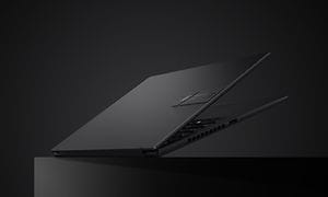 Svart halvöppen laptop som ser ut att sväva en bit över svart underlag mot svart bakgrund