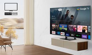Ett vardagsrum med stort fönster och naturutsikt med en TCL-TV på en vägghylla som visar menyval med filmer och appar