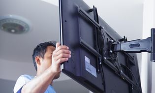En man monterar en TV på ett väggfäste.