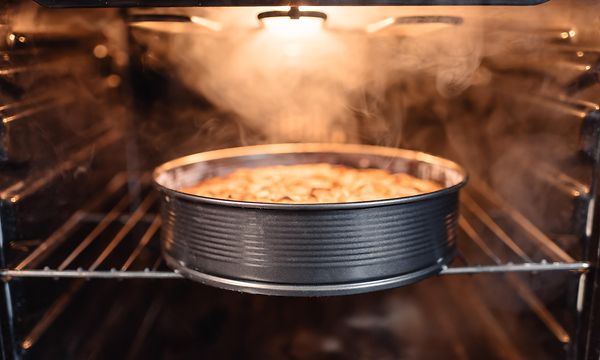 Kaka som steks i en rund form inne i en ugn med ljuset på och ånga inne i ugnen