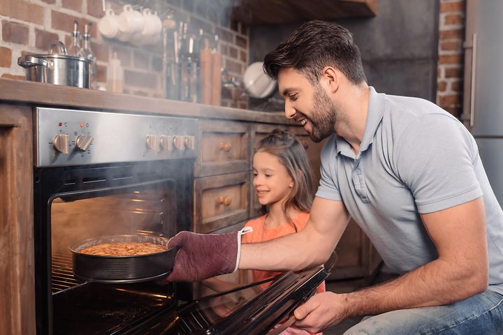 Far och dotter som ser glada ut tar ut en nybakad kaka från ugnen som ryker