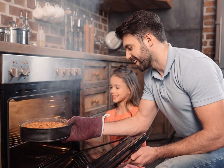 Far och dotter som ser glada ut tar ut en nybakad kaka från ugnen som ryker