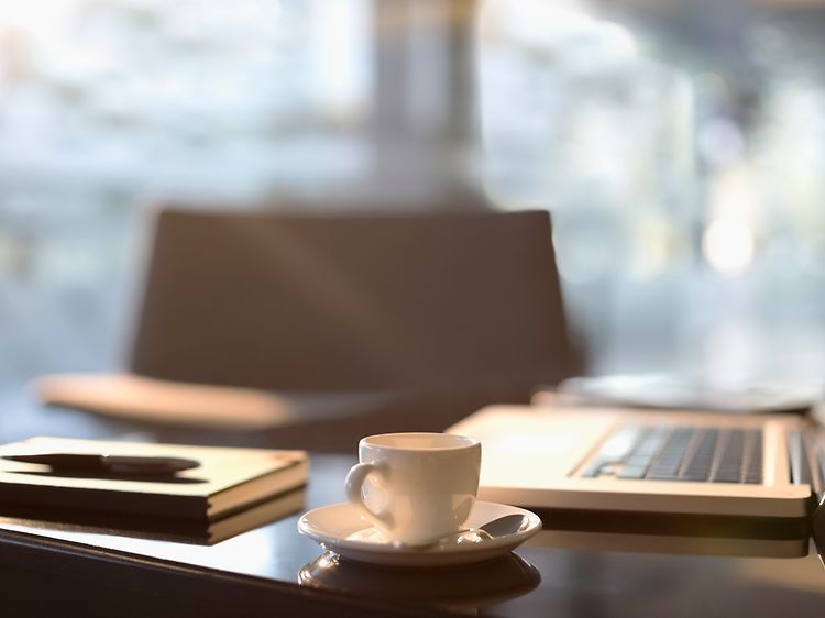 Kaffekopp ståendes bredvid en Macbook på ett skrivbord.