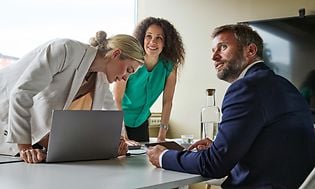 B2B - Två kvinnor och en man vid en bärbar dator i ett mötesrum och den ena kvinnan ser glad ut.