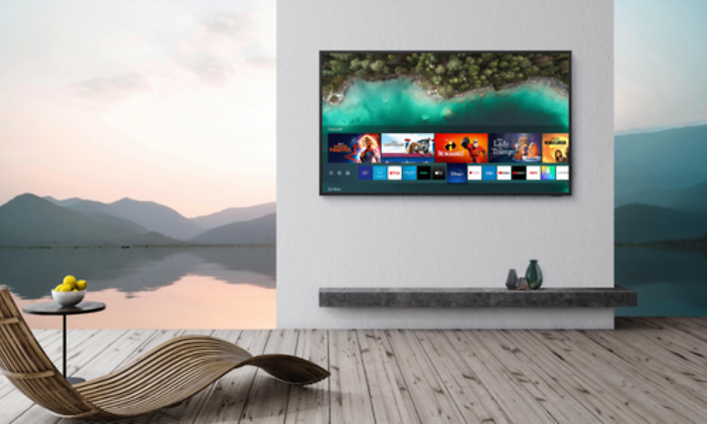 Samsung The Terrace på en vägg med en solstol bredvid med utsikt mot en sjö och berg efter solnedgång