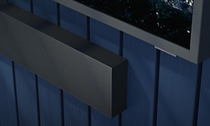 Närbild av hörnet av en soundbar på en blå vägg och hörnet av en TV-skärm fäst på väggen ovanför