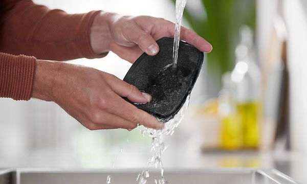 Tvättning av ett filter för stavdammsugare under rinnande vatten.