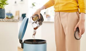 Person som tömmer dammbehållaren på en skaftdammsugare i soptunnan.