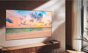 TV fäst på en vägg över en TV-bänk, som visar hav och himmel med moln, och ljus kommer in från fönstret utan att störa bilden