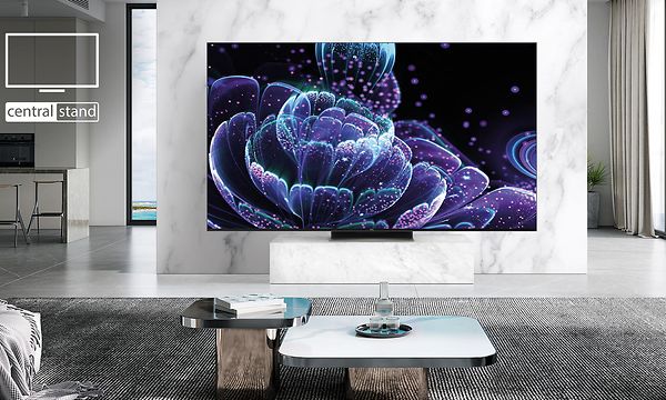 Stor TV-skärm som står på ett centraliserat stativ på en TV-bänk i stort, ljust vardagsrum 