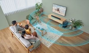 Vardagsrum och familj i en soffa som tittar på en TV som visar en motorcyklist medan illustrerade ljudvågor sprids i rummet
