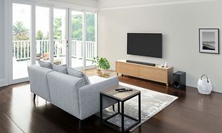 Vardagsrum med grå soffa och TV-bord framför en TV-skärm på en TV-bänk av trä och en soundbar under