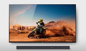 Skärm med motorcyklist i en öken och en soundbar som hänger på väggen under den