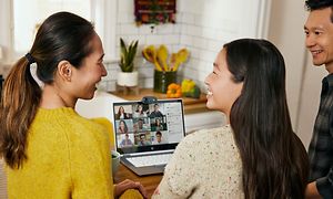 Asiatisk familj i ett kök som har ett videosamtal med flera andra på skärmen på en HP 2-in-1 Chromebook