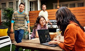 Familj med två tonåringar ocn en man och kvinna på en uteplats vid en grill med en Acer Spin Chromebook framför kvinnan
