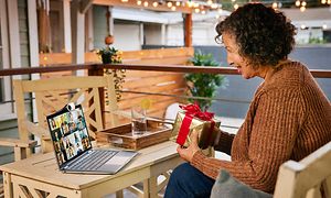 Kvinna i videosamtal ute på en veranda som håller en present med flera personer på skärmen på sin HP X360 Chromebook