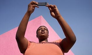 Kvinna som håller Pixel 6a med rosa byggnad och himmel bakom