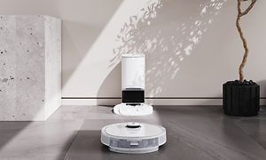 Automatisk tömningsstation på ett stengolv och robotdammsugare framför den
