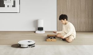 N8 PRO+ vit robotdammsugare bredvid en liten pojke som sitter på ett ljust golv med sina leksaker