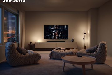 Samsung gaming-TV som visar en stad i kvällsmörker i ett vardagsrum med dämpad belysning över en soundbar och en TV-möbel